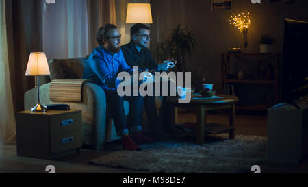Am Abend zwei Freunde Sitzen auf einem Sofa im Wohnzimmer und wettbewerbsfähigen Videospiele spielen. Sie schieben und schubsen Einander freundlich. Stockfoto