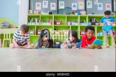 Gruppe von Vielfalt Kind legte sich auf den Boden und lesen Märchen Buch im Kindergarten Bibliothek, Kindergarten Schule Ausbildung Konzept. Stockfoto