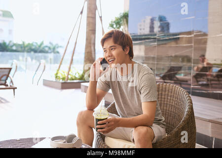 Asiatische Mann auf einem Telefon beim Sitzen draußen in den sonnigen Sommertag. Stockfoto