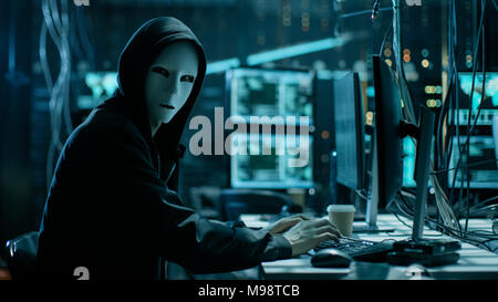 Maskierte Hacker ist mit Computer für die Organisation massive Verletzung der Datensicherheit Angriff auf Corporate Server. Sie sind in unterirdischen geheimen Ort Stockfoto