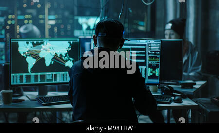 Zurück Blick auf Jugendliche Hacker arbeiten in Computer und infiziert mit dem Virus Daten Server der öffentlichen Infrastrukturen. Sein Versteck ist Dunkel mit Monitoren Stockfoto
