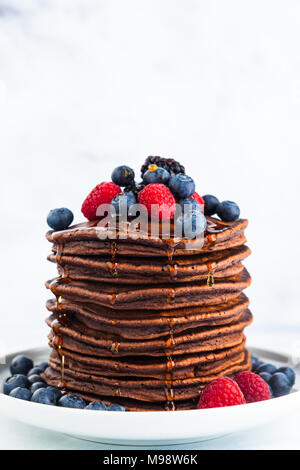 Fließende Ahornsirup auf einem Haufen Schokolade Pfannkuchen mit frischen Beeren. Morgen gesundes Frühstück Stockfoto