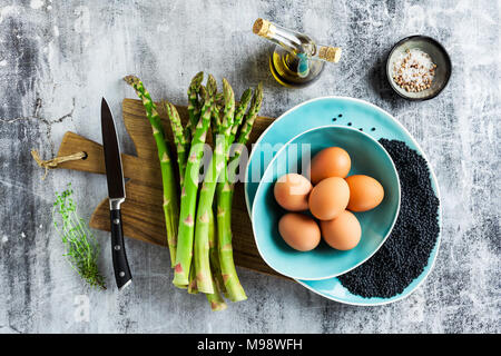 Zutaten für das Kochen von Spargel, schwarze Linsen, Olivenöl und Eiern auf der Tabelle auf grauem Stein Tabelle Stockfoto