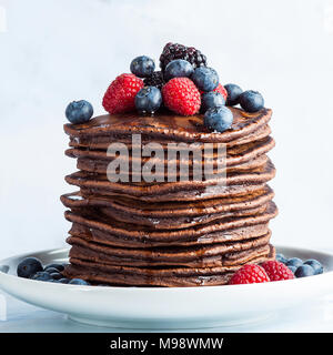 Fließende Ahornsirup auf einem Haufen Schokolade Pfannkuchen mit frischen Beeren. Morgen gesundes Frühstück Stockfoto