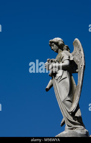 Stein weiblicher Engel mit Blumen. Weibliche Engel isoliert mit blauer Himmel. Stockfoto