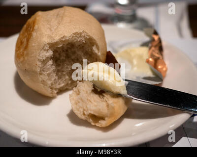 Frisch gebackene Brötchen und Butter auf eine weiße Platte mit einem Messer Stockfoto