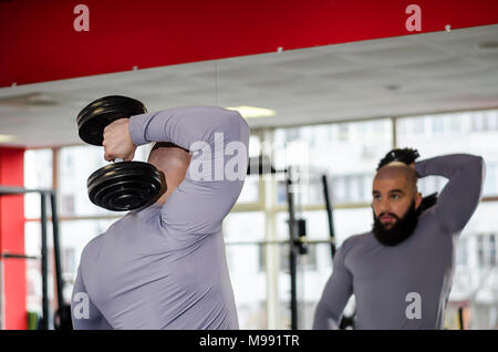 Starke männliche Athlet, Kurzhanteln, an Training Ergebnisse im Spiegel zu betrachten Stockfoto
