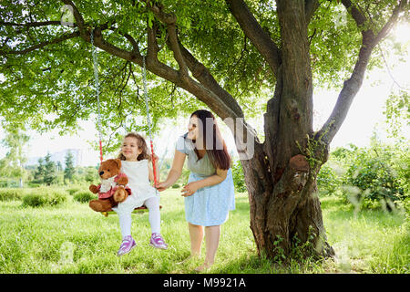 Mutter rollt auf einer Schaukel im Park im Sommer. Kinder-Schutz-Tag. Stockfoto