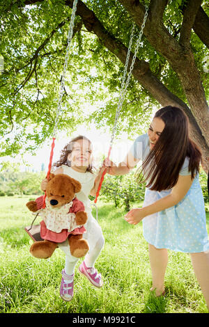 Mutter rollt auf einer Schaukel im Park im Sommer. Kinder-Schutz-Tag. Stockfoto