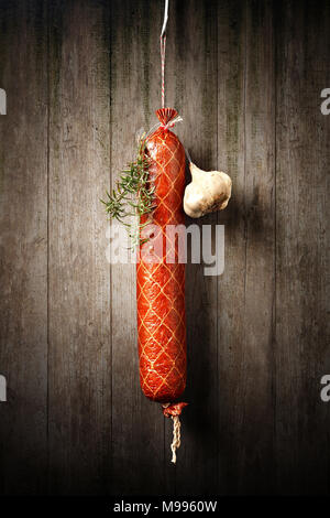 Salami Wurst gehängt mit Knoblauch und Rosmarin gegen einen alten rustikalen hölzernen Wand trocknen Stockfoto