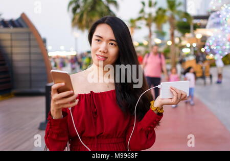 Mädchen mit Handy während des Ladevorgangs auf dem Power Bank im Freien Stockfoto