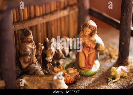 Eine antike bemalt Porzellan Krippe (kinderkrippe) mit Maria, Josef und dem Jesuskind in einer Krippe, in einem hölzernen stabil. Stockfoto
