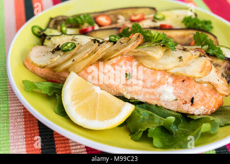 Lachs filet Steak im Ofen gebacken mit Salat und gebackene Kartoffeln in Scheiben geschnitten - auf der grünen Platte mit Jalapenos und Zitrone serviert. Stockfoto