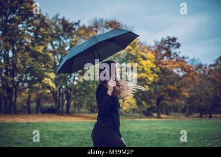 Glückliche junge Frau mit Schirm wandern in herbstlichen Park Stockfoto