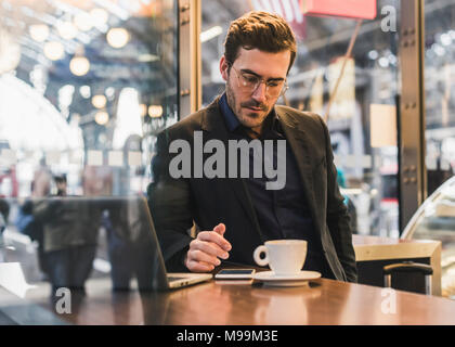 Junge Unternehmer in einem Café am Bahnhof mit Tasse Kaffee, Laptop und Handy Stockfoto