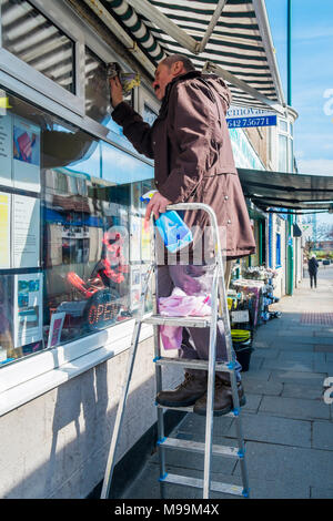 Mann auf einer Leiter Reinigung ein Schaufenster für ein kleines Unternehmen in North Yorkshire Stockfoto