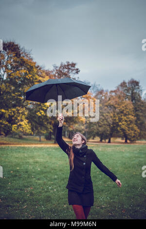 Glückliche junge Frau tanzen mit Regenschirm im herbstlichen Park Stockfoto