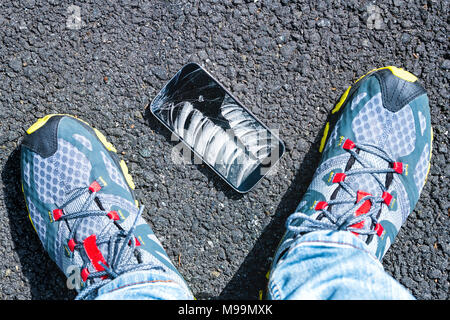 Person auf Asphalt mit gebrochenen Telefon Bildschirm des Smartphones fiel auf den Boden, Schuhe Sneakers Stockfoto