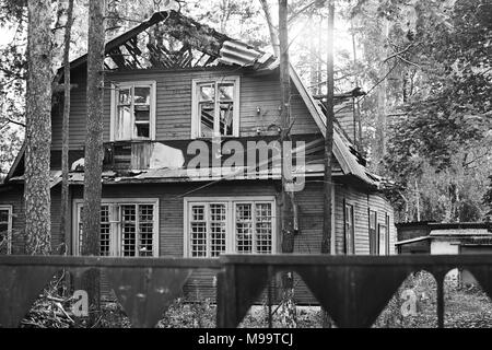 Ruine der alten Holzhaus unter den Bäumen und metall Zaun um. Schwarz und Weiß Stockfoto
