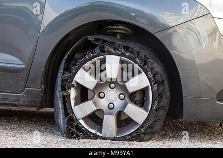 Sie zerstörte Reifen geblasen mit explodierte, geschreddert und beschädigte Gummi auf modernem SUV Automobil. Flache flache Reifen auf einer Leichtmetallfelge, riss öffnen Stockfoto