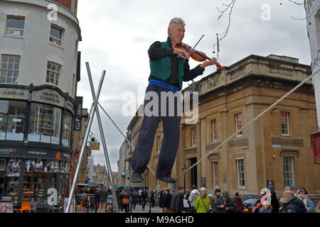 Bristol, UK. 24. März 2018. Ein Nachmittag der Straßenunterhaltung in Wein Straße, Bristol. Eine Performance von slacklining zwischen zwei Pfosten durch die Person spielt eine Violine und gekonnt Balancing beim Gehen auf ein Seil in middair unterbrochen und von Zuschauern verfolgt werden. Robert Timoney/Alamy/live/Aktuelles Stockfoto