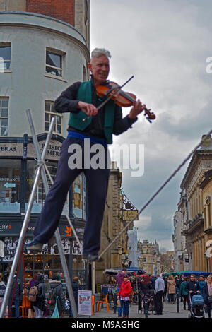 Bristol, UK. 24. März 2018. Ein Nachmittag der Straßenunterhaltung in Wein Straße, Bristol. Eine Performance von slacklining zwischen zwei Pfosten durch die Person spielt eine Violine und gekonnt Balancing beim Gehen auf ein Seil in middair unterbrochen und von Zuschauern verfolgt werden. Robert Timoney/Alamy/live/Aktuelles Stockfoto