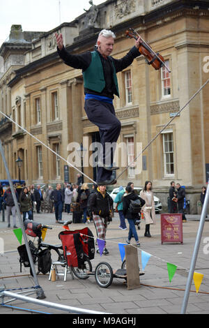 Bristol, UK. 24. März 2018. Ein Nachmittag der Straßenunterhaltung in Wein Straße, Bristol. Eine Performance von slacklining zwischen zwei Pfosten durch die Person spielt eine Violine und gekonnt Balancing beim Gehen auf ein Seil in middair unterbrochen und von Zuschauern verfolgt werden. Robert Timoney/Alamy/live/Aktuelles Stockfoto