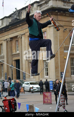 Bristol, UK. 24. März 2018. Ein Nachmittag der Straßenunterhaltung in Wein Straße, Bristol. Eine Performance von slacklining zwischen zwei Pfosten durch die Person spielt eine Violine und gekonnt Balancing beim Gehen auf ein Seil in middair unterbrochen und von Zuschauern verfolgt werden. Robert Timoney/Alamy/live/Aktuelles Stockfoto