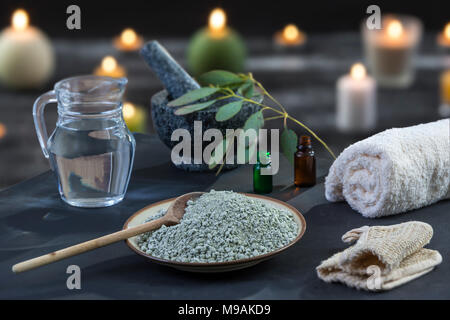 Spa Zusammensetzung auf schwarzem Holz- Hintergrund. Weiß gerollt , steigen Sie Kerzen, grüne Kräuter, Eukalyptus Ton Maske für Gesicht und Körper, Stockfoto