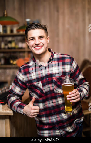 Schöner Mann hält ein Glas Bier mit Daumen hoch in einem Pub Stockfoto