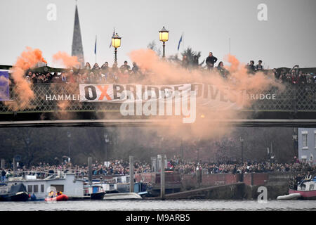 Flares sind Sie in der Nähe ein "Oxbridge veräußern" Banner auf die Hammersmith Bridge während der Männer Boot Rennen lassen auf der Themse, London. Stockfoto