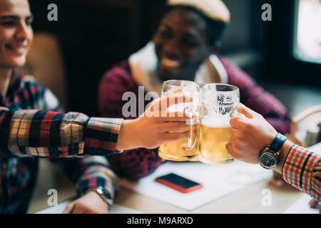 Glücklich lächelnde männliche Freunde klirren mit Bierkrügen in Pub Stockfoto