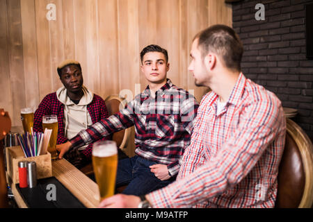 Freunde traf nach einem harten Tag. Drei fröhlichen Freund clink Bier an der Bar und trinken ein Bier. Stockfoto