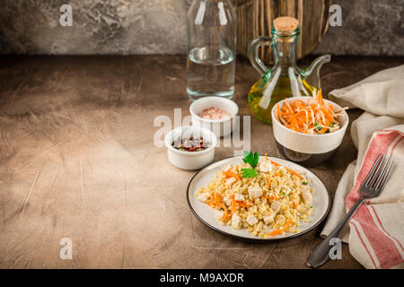 Bulgur Pilaw mit Huhn in einen Teller und eine Schüssel Krautsalat auf braunem Hintergrund konkrete Stockfoto