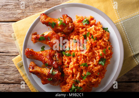 Porcion der Afrikanischen Jollof Reis mit Fried Chicken wings Close-up auf einem Teller auf dem Tisch. horizontal oben Ansicht von oben Stockfoto