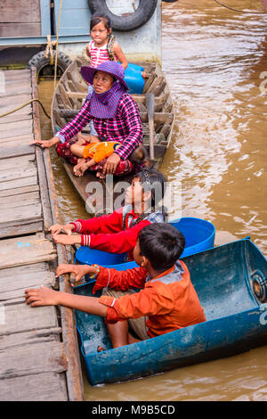 Zwei junge Kinder schweben in Kunststoff Fässer neben ihrer Mutter mit zwei kleinen Kindern, für das Geld von Touristen an der schwimmenden Dorf am Fluss Siem Reap zu betteln, Kambodscha Stockfoto