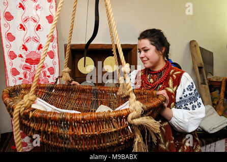 Frau, die in der ukrainischen native Kleid rockt ein traditionelles Gestell mit einem Baby. Wiederaufbau der ukrainischen Traditionen. 23. März 2018. Kiew, Ukraine Stockfoto