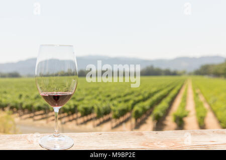 Ein Glas Rotwein auf einem Deck Geländer mit Blick auf Reihen von Weinstöcken stretching durch einen Weinberg im Hintergrund Stockfoto