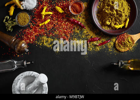 Kochen mit frischen Gewürze mit Mörtel und kleine Schalen von Spice auf einem Schwarzen Tisch mit Pulver verschütten auf seiner Oberfläche, Ansicht von oben mit copysp Stockfoto