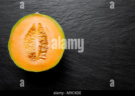 Die Hälfte der Hami melone Frucht auf schwarzem Stein Hintergrund Oberfläche mit freier Speicherplatz Stockfoto