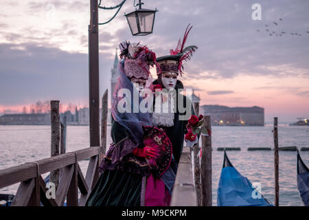 Romantisches Paar in Kostümen und Masken stehen mit Zurück zu den Grand Canal, Gondeln und San Giorgio im Hintergrund, während der Karneval von Venedig Stockfoto