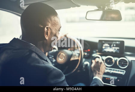 Rückspiegel eines jungen afrikanischen Geschäftsmann ändern Radio Stationen während der morgendlichen Fahrt zum Arbeitsplatz in der Stadt zu arbeiten Stockfoto