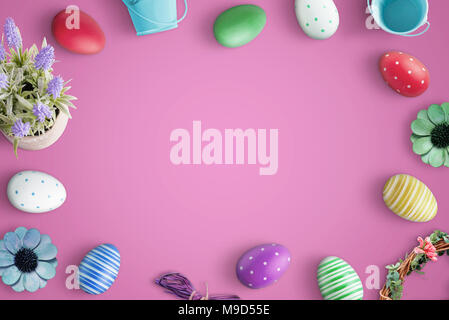 Blick von oben auf die Frohe Ostern Komposition mit Flach bunte Eier und Dekorationen. Rosa Hintergrund. Stockfoto