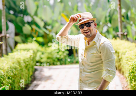 Junger Mann in eine Sonnenbrille tragen gelbe Hut und legere Kleidung Spaß im sonnigen Tag. Tropischen Hintergrund. Stockfoto