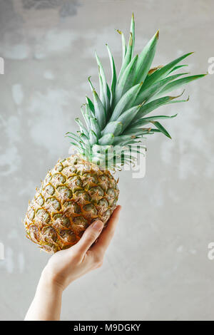 Weibliche Hand, die eine reife Ananas Obst auf einem grauen konkreten Hintergrund Stockfoto