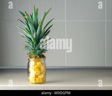 Frische saftige Ananas Stücke in einem Glas auf dem Küchentisch gegen Grau rile Hintergrund Stockfoto