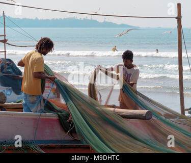 Weligama, Sri Lanka, 2018-01-23: Loсal Fischer stehen auf Boot und Entwirren, Bereich Fischernetz, im Hintergrund Ocean Beach. Stockfoto