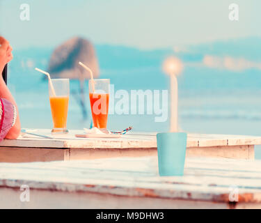 Frau hand, zwei Gläser mit frischem Obst, Säften, brennende Kerze auf hölzernen Tisch im Cafe am Strand. Konzept der Ferienhäuser, Reisen, Romantik, Urlaub Stockfoto