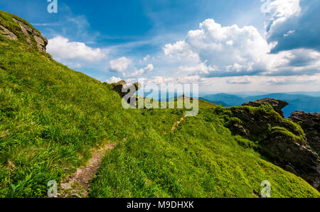 Pfad zu den Rand eines Hügels. schönen bergigen Landschaft mit grasbewachsenen Hügel und riesige Felsbrocken unter. schönem Wetter mit blauem Himmel und einige Wolken Stockfoto