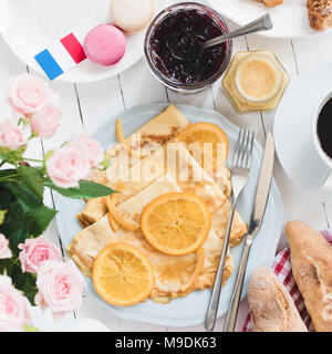 Französisches Frühstück Crepes Suzette, Baguette, Kaffee und Marmelade auf weiße Holztisch. French Flag, Macarons, Marmelade, Honig und Rosen zur Seite Stockfoto
